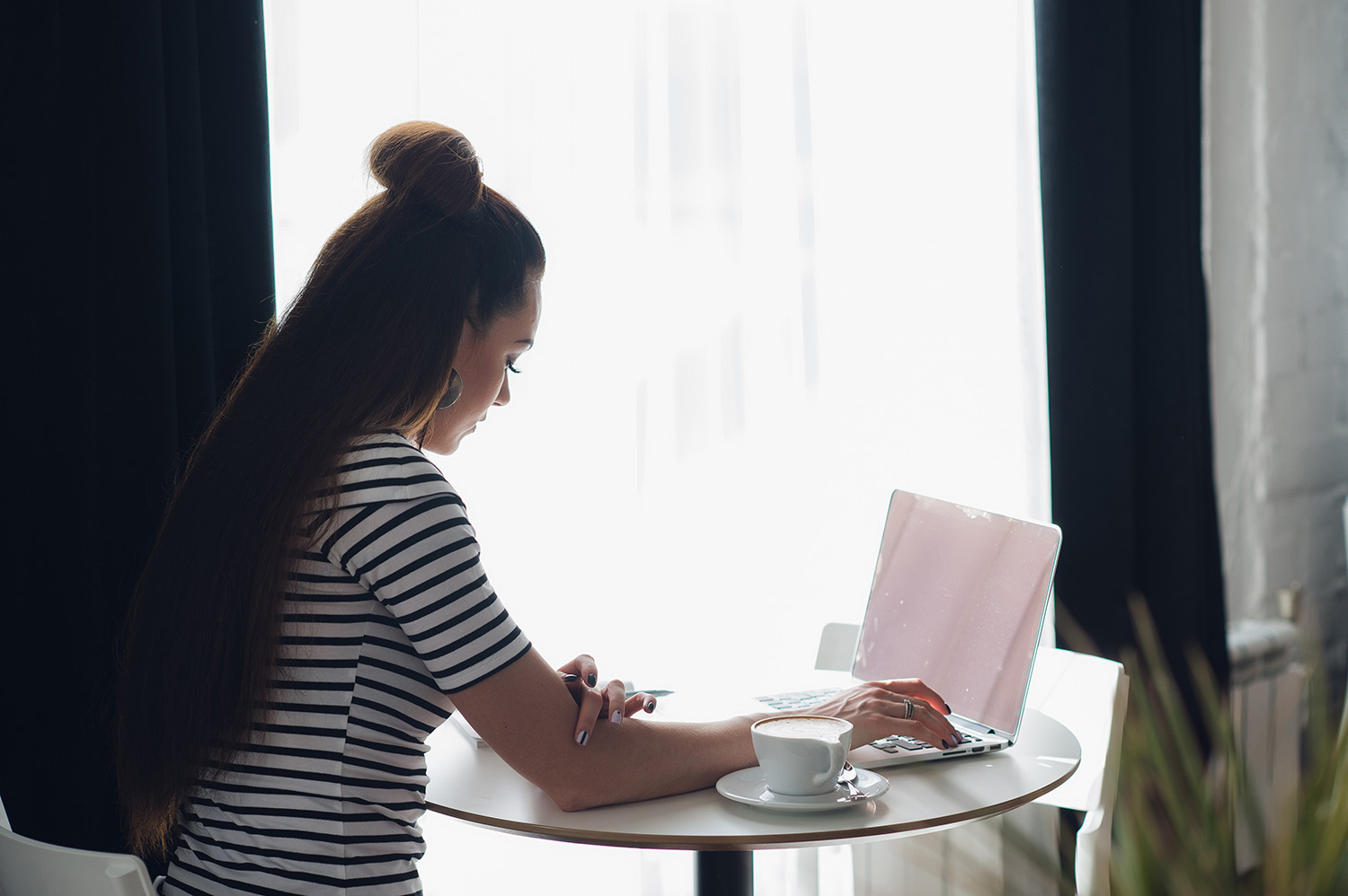 Overhead view of an executive woman typing in her laptop. View from the back of a female sitting at the table with a cup of coffee and computer.